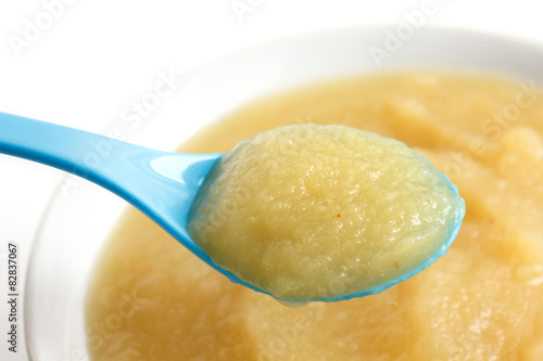 White dish of apple sauce with blue baby spoon.