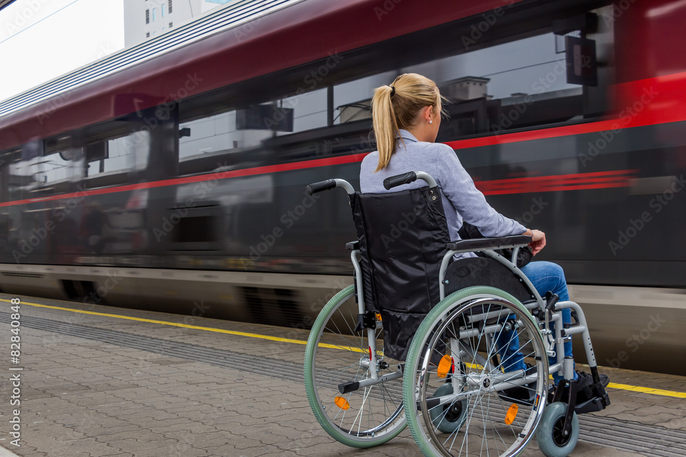 Frau sitzt in einem Rollstuhl auf einem Bahnhof