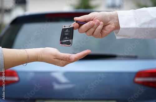 car dealer gives the customer the car keys with car in backgorun