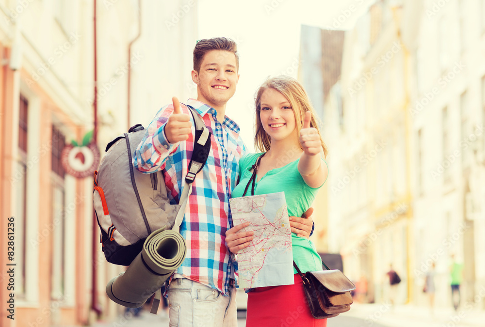 smiling couple with map and backpack in city