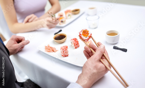 close up of couple eating sushi at restaurant