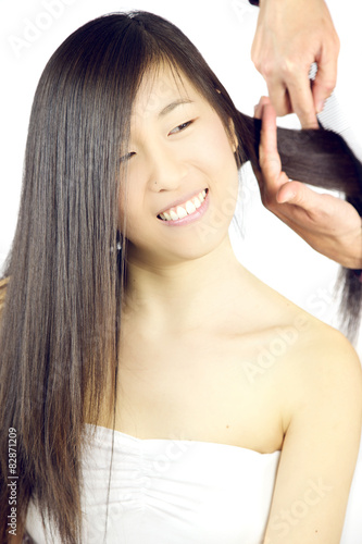 Cute asian girl with long hair getting combed by stylist