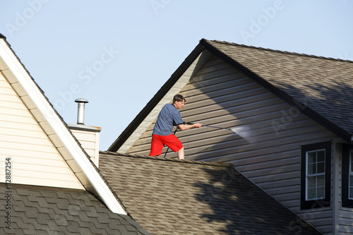 Man on the roof of a house pressure washing the vinyl siding.