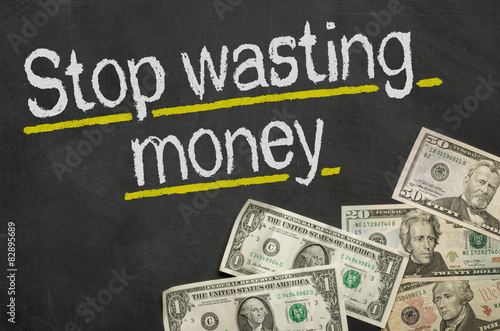 Text on blackboard with money - Stop wasting money