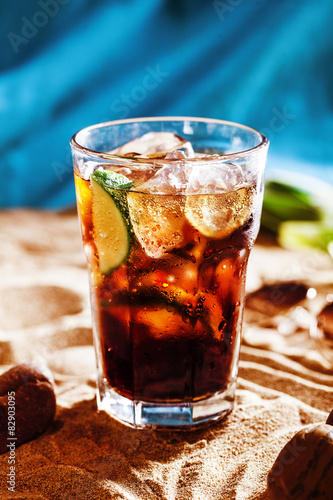 Photography juicy cocktail with lime and cola in a sweaty glass the sand