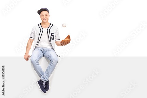 Young man playing with a baseball seated on panel