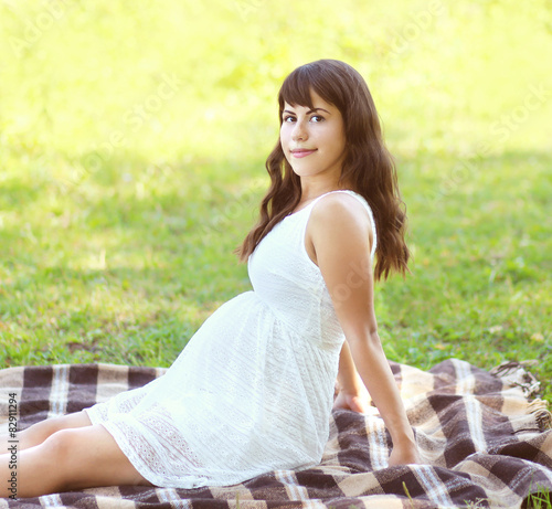 Beautiful pregnant young woman lying on the grass in summer day
