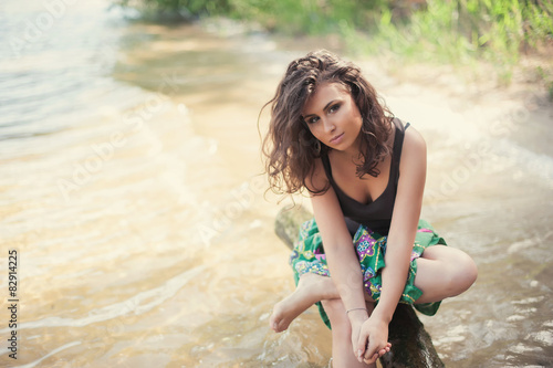 Beautiful brunette woman sits on a background of water