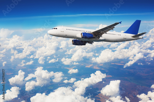 Commercial airliner flying above clouds with blue sky.
