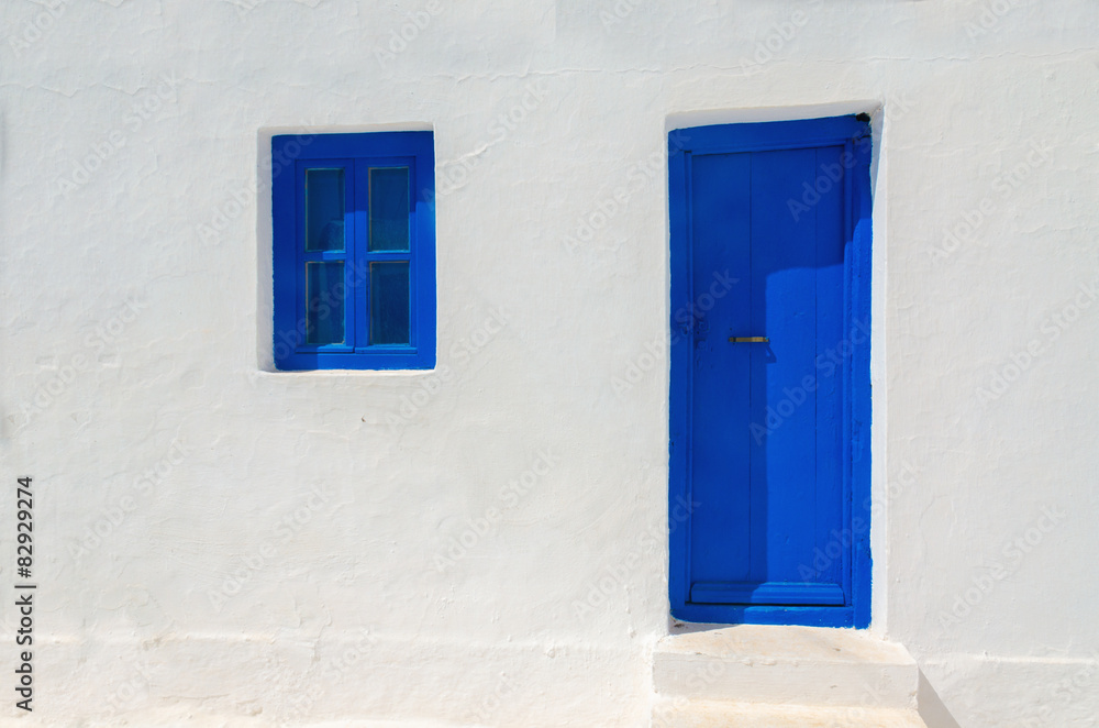 Fototapeta premium Iconic blue wooden door and window against clear white wall. Typ