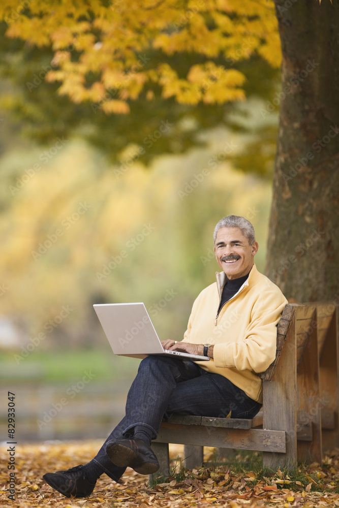 African man using laptop on park bench in autumn African man using laptop on park bench in autumn