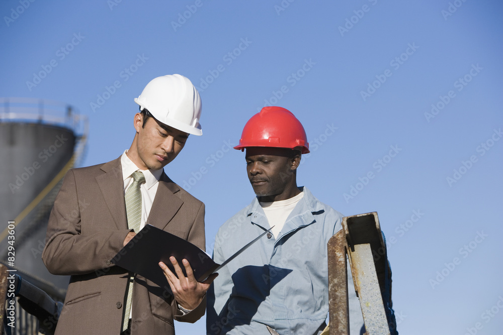 Multi-ethnic businessman and construction worker looking at paperwork Multi-ethnic businessman and construction worker looking at paperwork