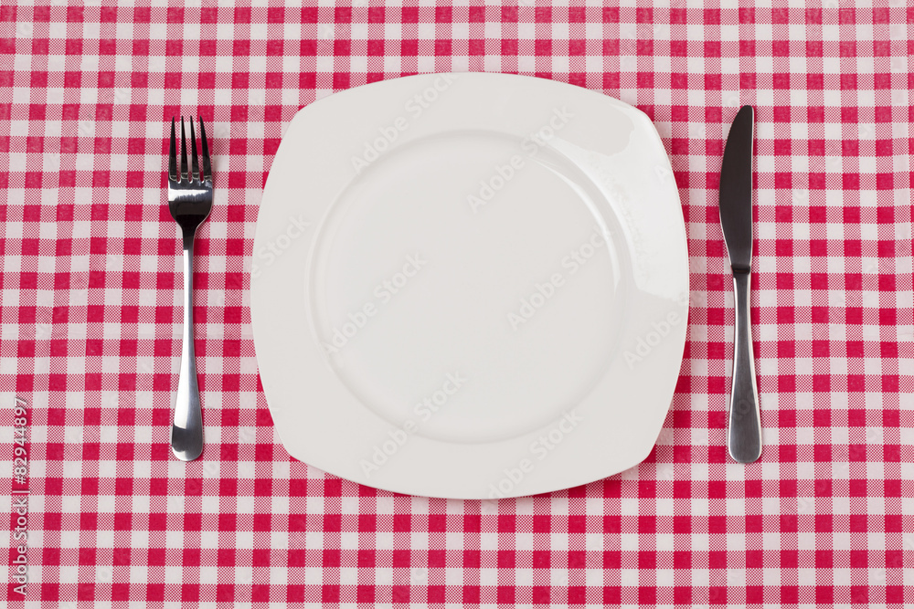 Empty plate setting with plate, knife and fork on red gingham Empty plate setting with plate, knife and fork on red gingham