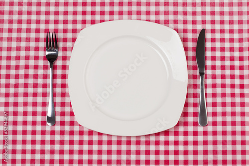 Empty plate setting with plate, knife and fork on red gingham 