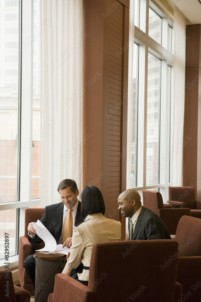 Multi-ethnic business people reviewing paperwork in lobby Multi-ethnic business people reviewing paperwork in lobby