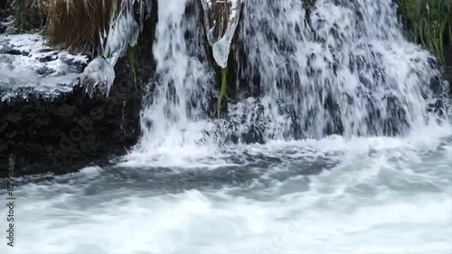 Water flows down frozen rocks and grass into the river