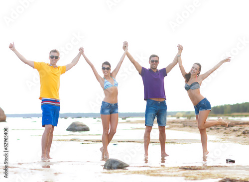 group of happy friends holding hands on beach