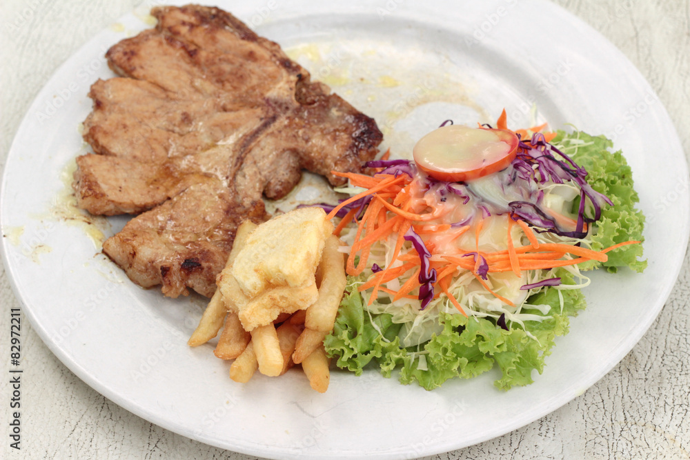 steaks and vegetable salad with french fries.