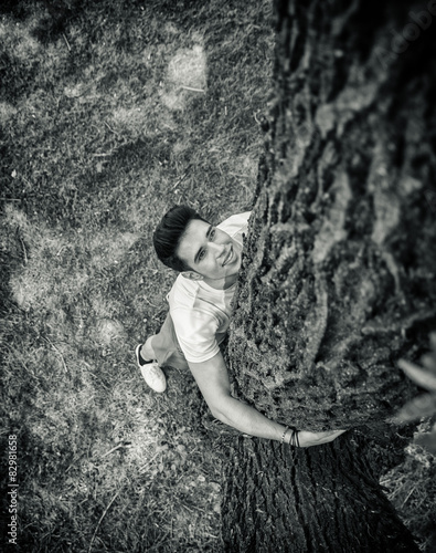 Smiling young man hugging a tree, looking up