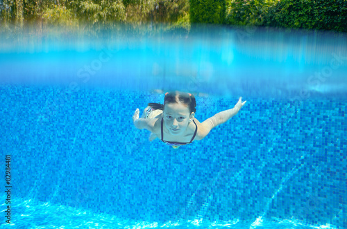 Happy child swims in pool underwater, active kid swimming