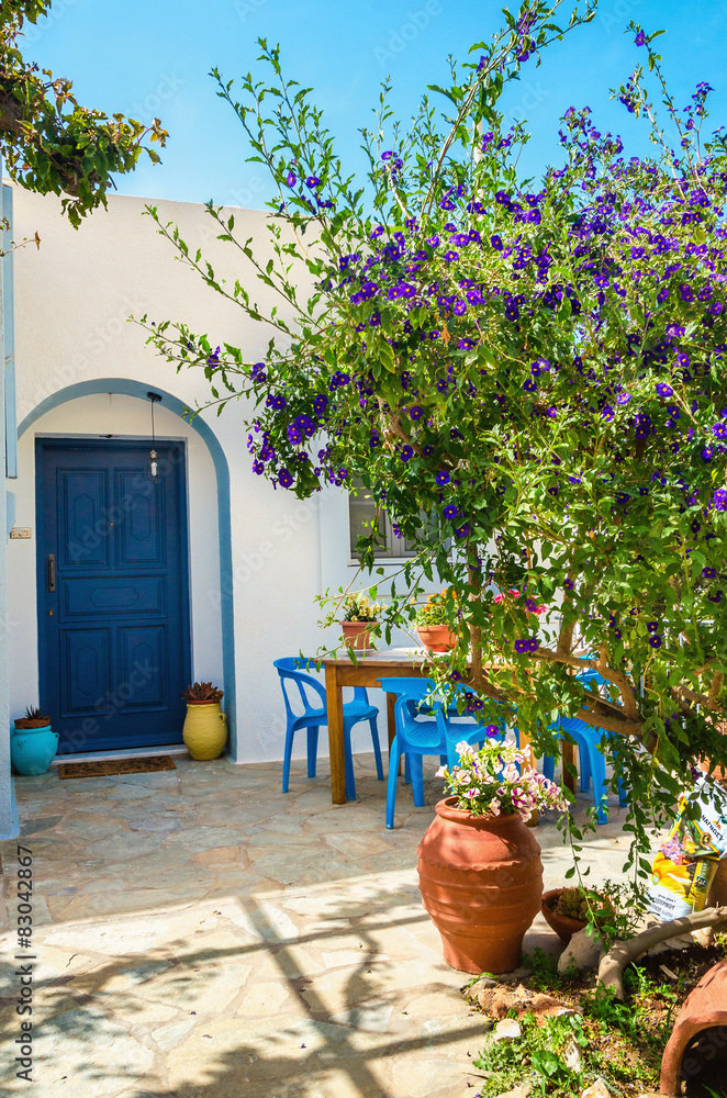 Entry to typical Greek house with blue dores and green trees in