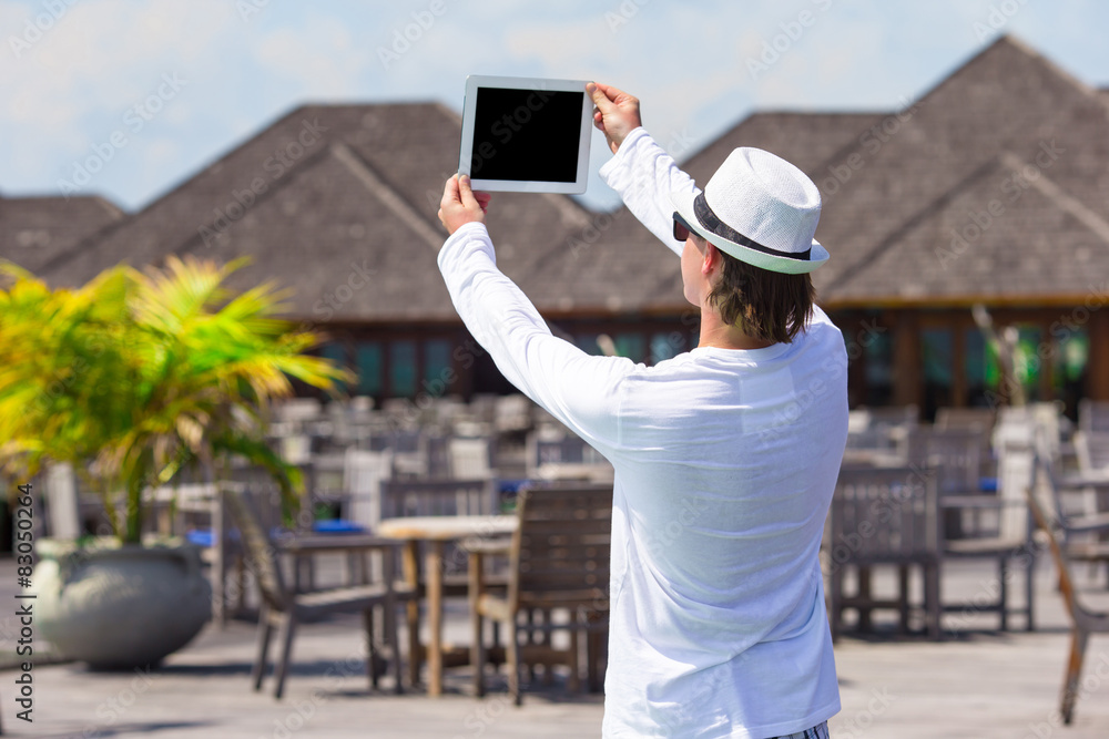 Young man make a photo on tablet computer at tropical beach 