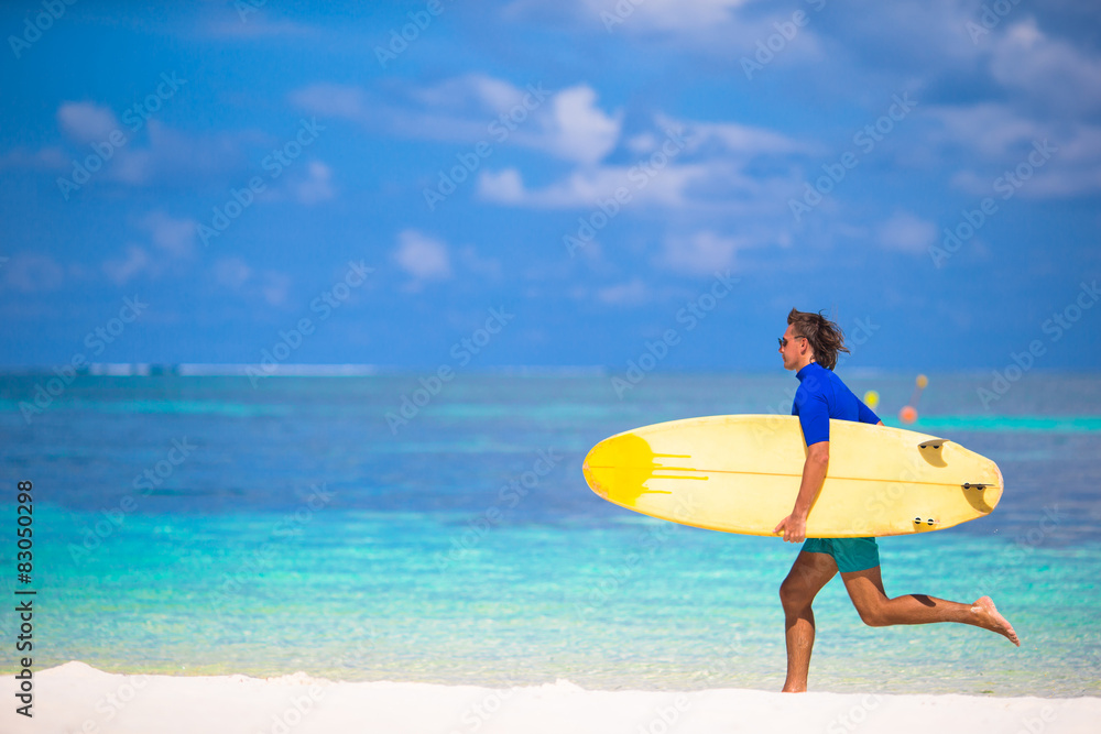 Happy young surf man runing at the beach with a surfboard