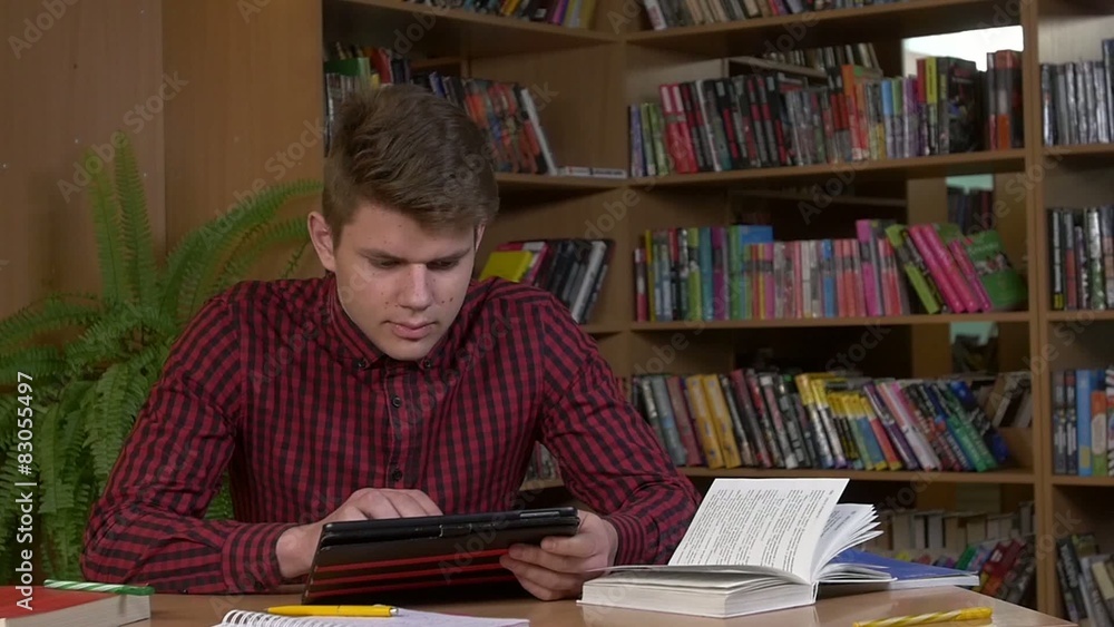 Student using his digital tablet in a library, preparing for Student using his digital tablet in a library, preparing for