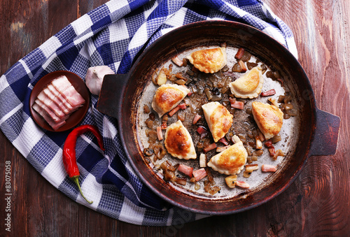 Fried dumplings with onion and bacon in frying pan, on wooden table background