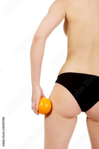 Female buttocks and orange in hand.