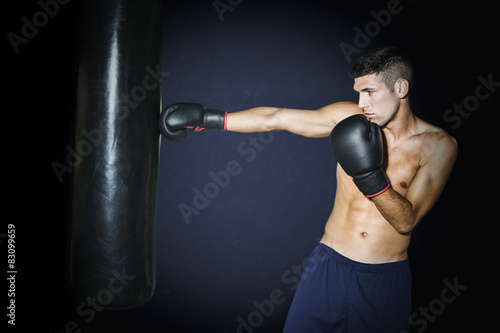 Muscular boxer training with punching bag at gym