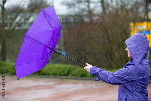 Eine Frau kämpft mit dem Regenschirm gegen den Sturm in Violett