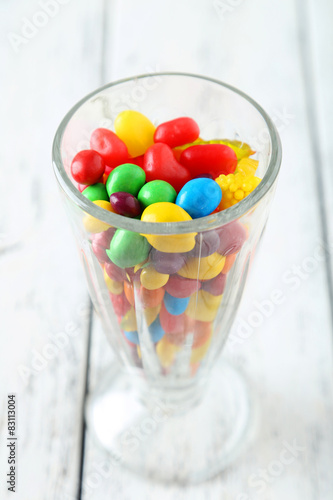 Colorful candies in glass on white wooden background