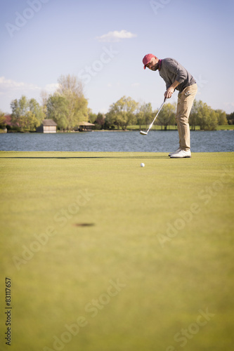 Male golf player putting on green.