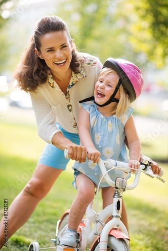 Laughing mother and daughter learning how to ride a bike