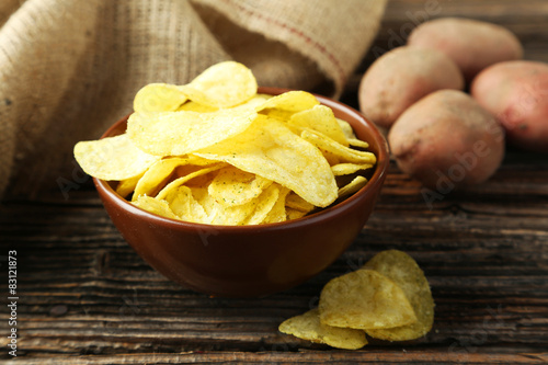 Potato chips in bowl on brown wooden background