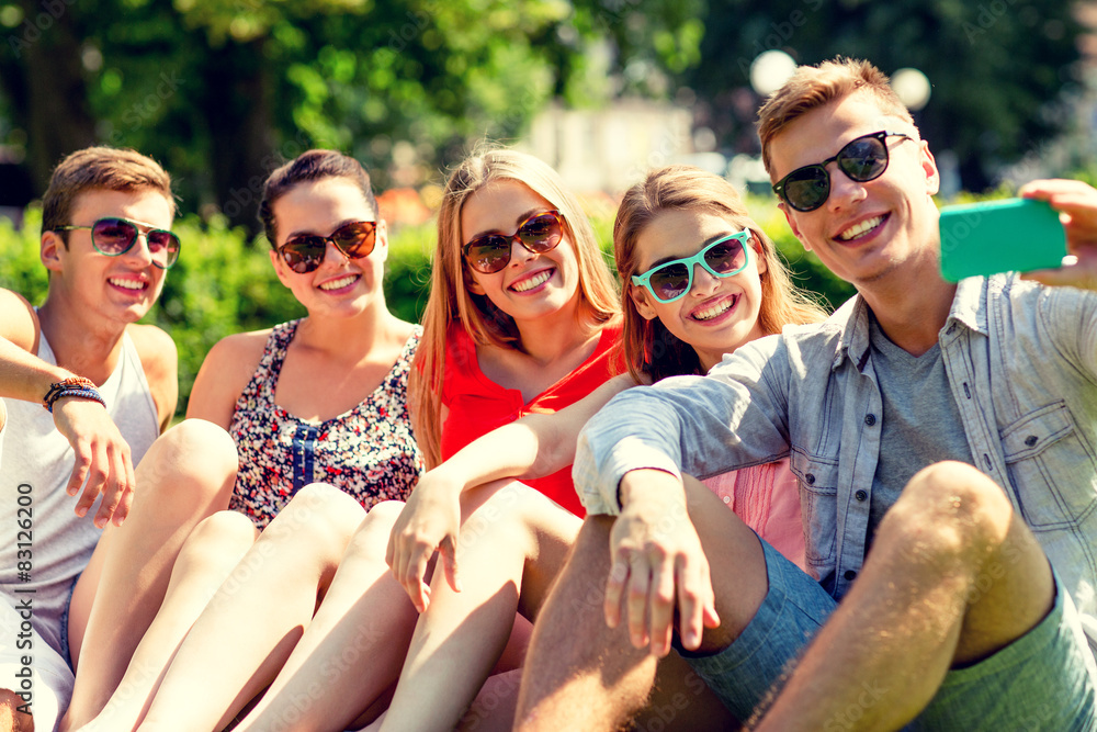 smiling friends with smartphone sitting on grass smiling friends with smartphone sitting on grass