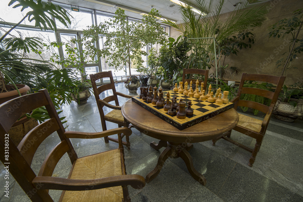 Chessboard on table with chairs in a hall with trees