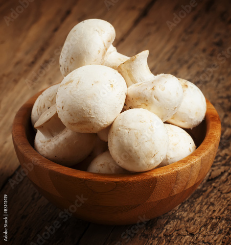 White mushrooms in a bowl on wooden table, selective focus
