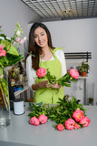 cheerful young woman florist selling flowers in flower shop