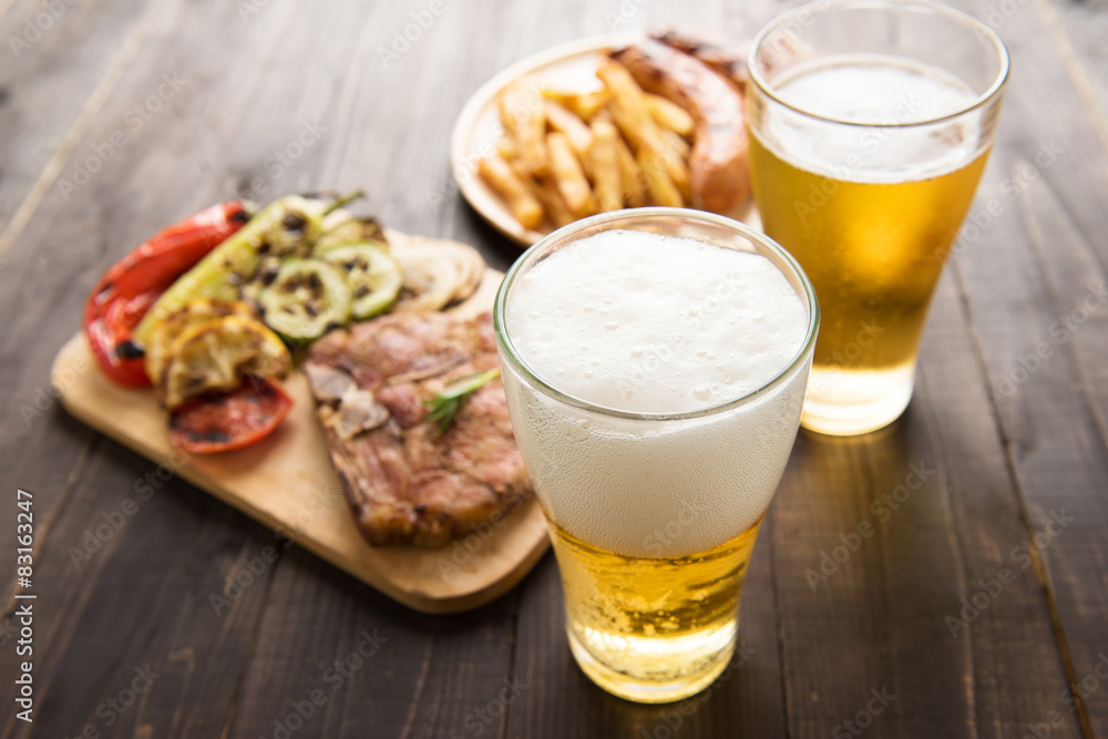 Beer in glass with gourmet steak and french fries on wooden 