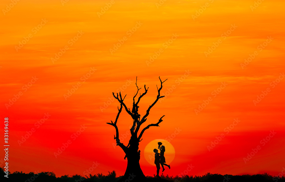 Silhouette of couple in love with big sunset and dead tree.