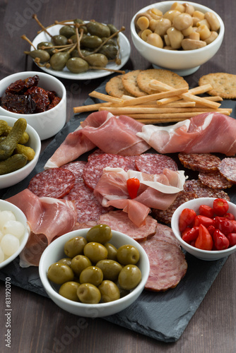 deli meat snacks, sausages and pickles on a dark wooden table