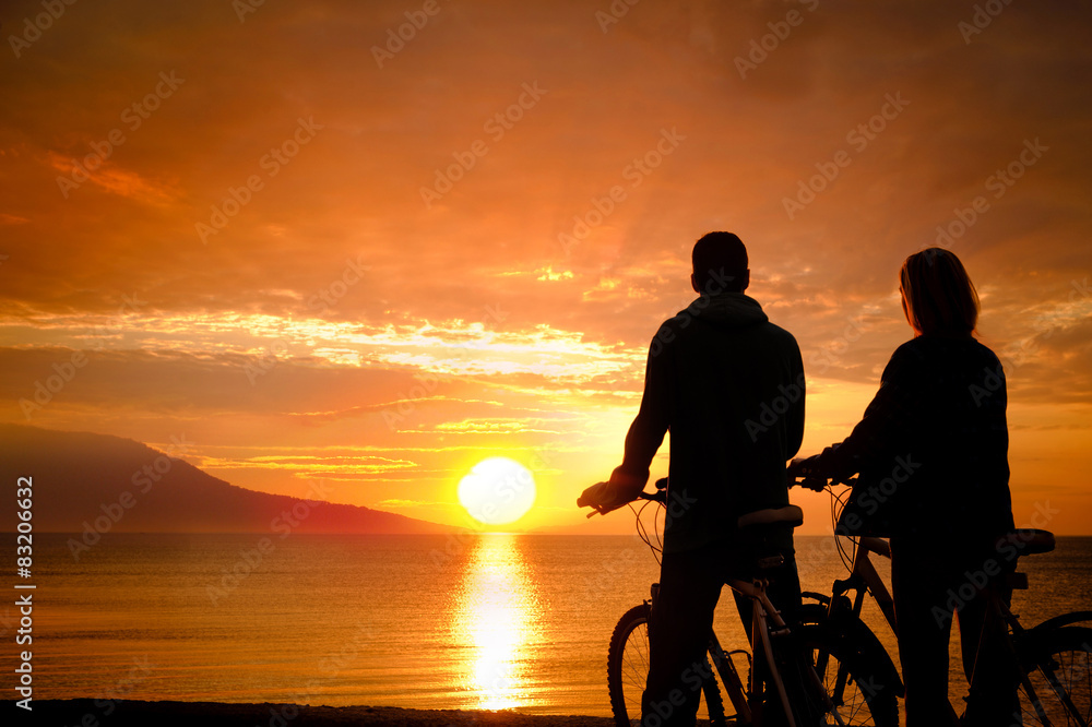 Couple of cyclists at the beach at sunset.