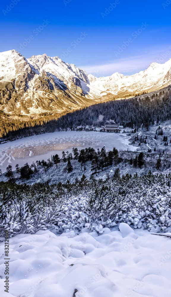 Vertical panorama of winter mountains, lake and cottage