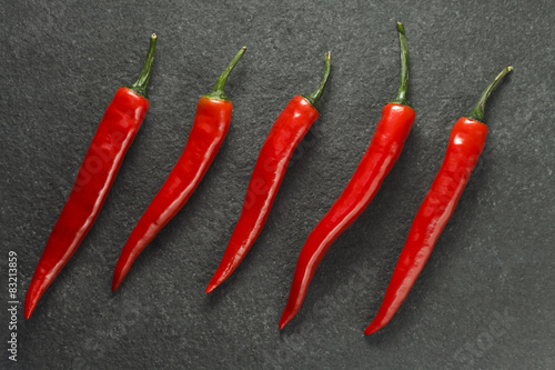 Five red chilli peppers on dark grey limestone