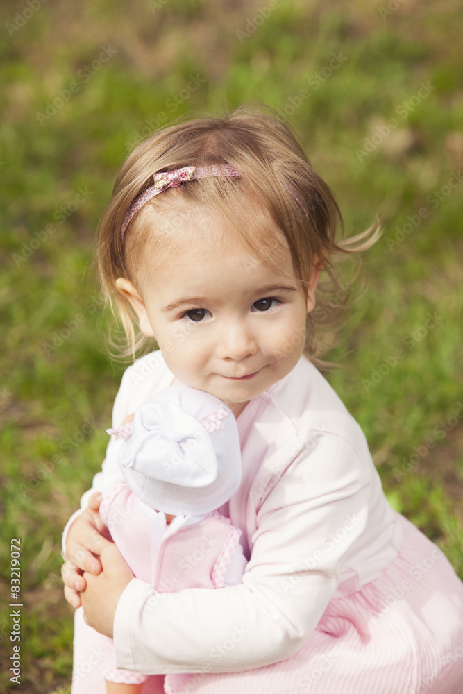 Cute little girl holding a doll baby outdoors Cute little girl holding a doll baby outdoors