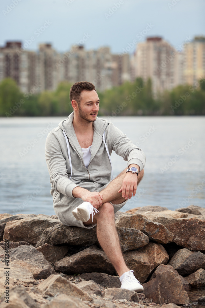 Attractive man is sitting at the water. Guy sitting on the river