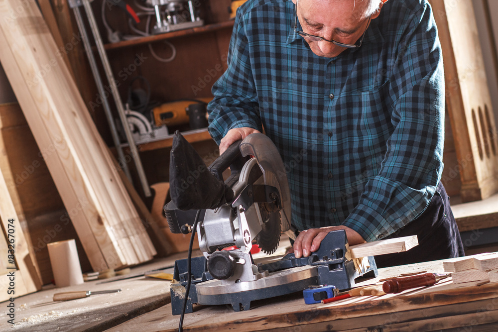 Senior carpenter cutting wooden plank with circular saw in his workshop. Senior carpenter cutting wooden plank with circular saw in his workshop.