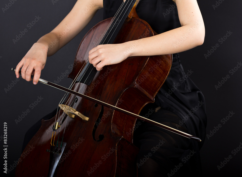 A young girl plays the cello in the dark. Hands on cello A young girl plays the cello in the dark. Hands on cello